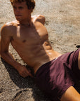 Man lying on a sandy surface wearing purple swim shorts