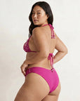 Woman wearing a pink sustainable bikini against a plain background