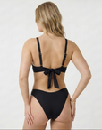 Woman wearing a sustainable black bikini with a bow detail on a white background