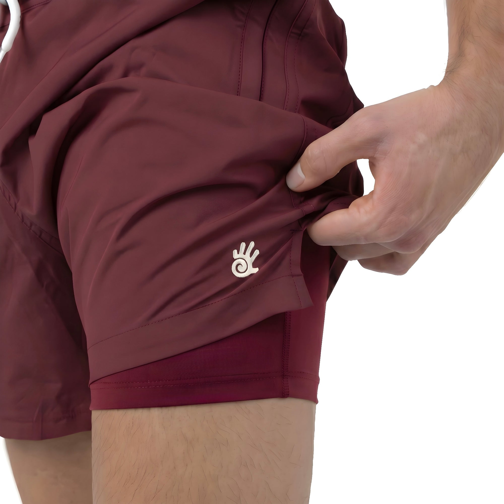 Burgundy men's swim shorts with a logo on a white background. The shorts are being lifted up slightly to show the anti-chafe swimwear lining. 